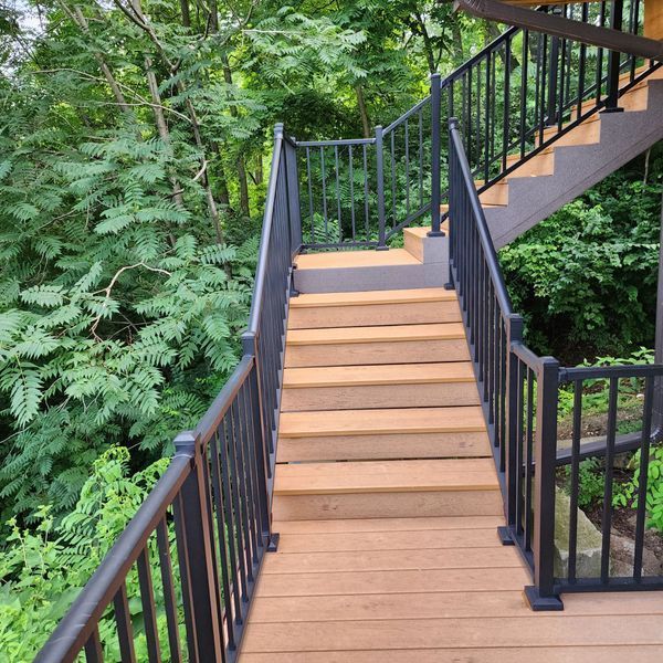 Wooden outdoor staircase with black metal railings ascending through lush green foliage.