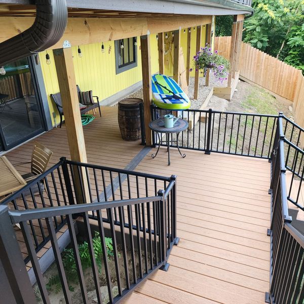 Wooden deck with black railings, stairs, and a yellow house.