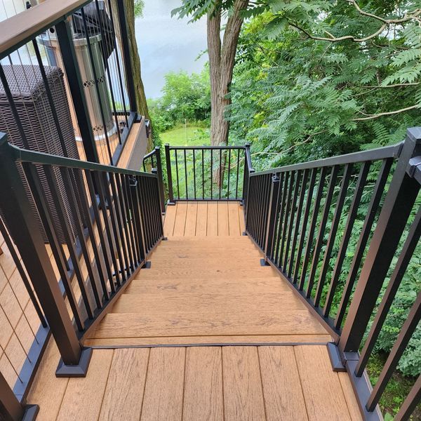 Wooden deck stairs with black railing, leading down to a green outdoor area.
