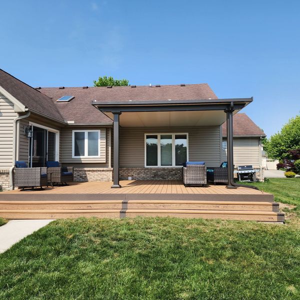 Backyard deck with a covered patio, beige siding, and green grass.