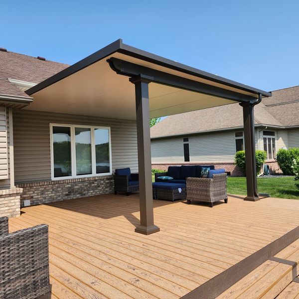 Patio with brown pergola and outdoor seating on a wooden deck next to a house.