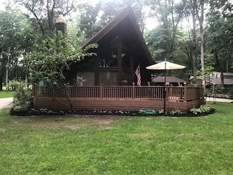 A-frame house with a brown deck, surrounded by green grass and trees, and an American flag.