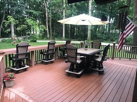Deck with outdoor furniture: chairs, table, umbrella, and American flag. Trees in the background.