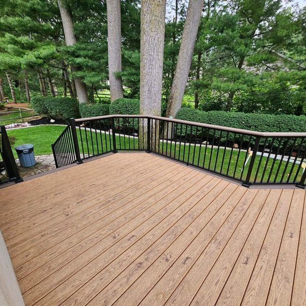 Wooden deck with black railings overlooking a green yard and trees.