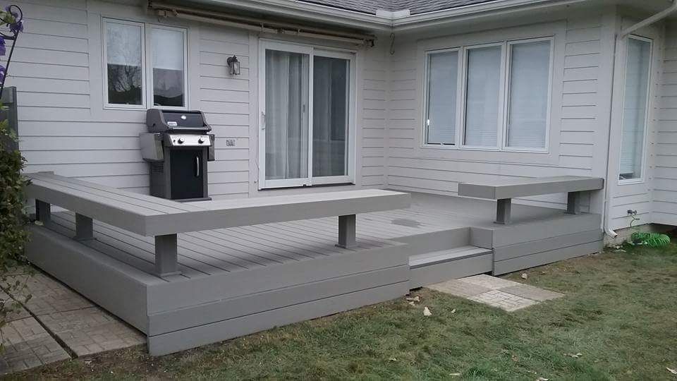 Gray deck with built-in benches, steps, and grill against a white house with sliding glass door and windows.