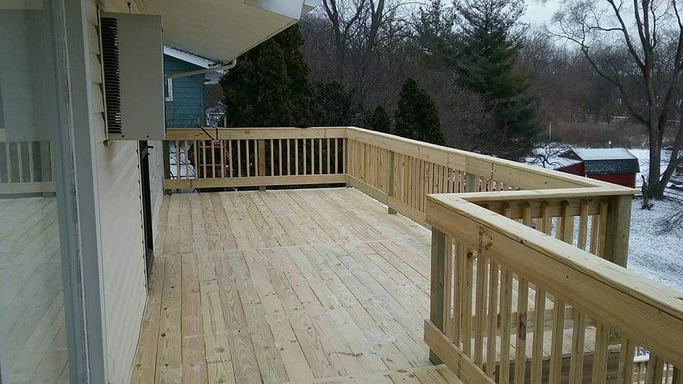 Wooden deck with railing, snowy yard, and a house.