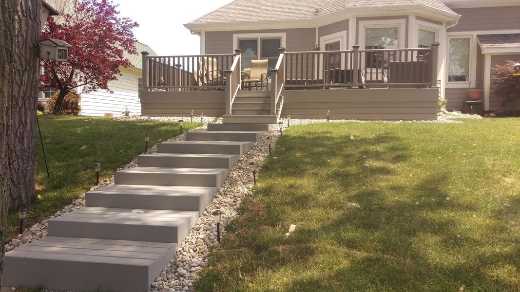Gray concrete steps leading up to a wooden deck with railing; house in the background.