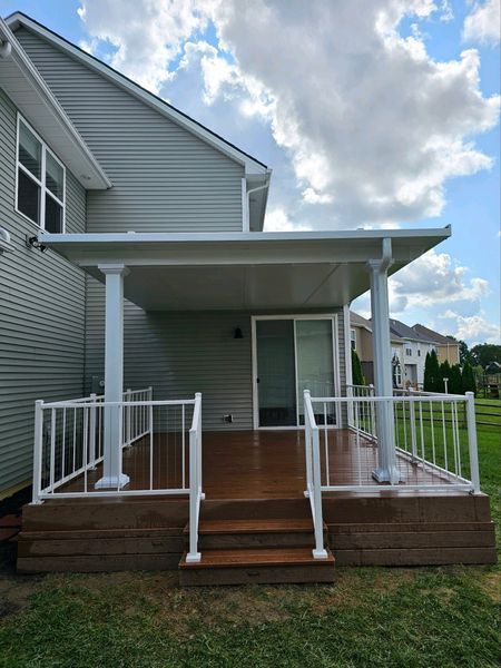 Backyard deck with white pillars, railing, and a roof, wooden deck, and a sliding glass door.