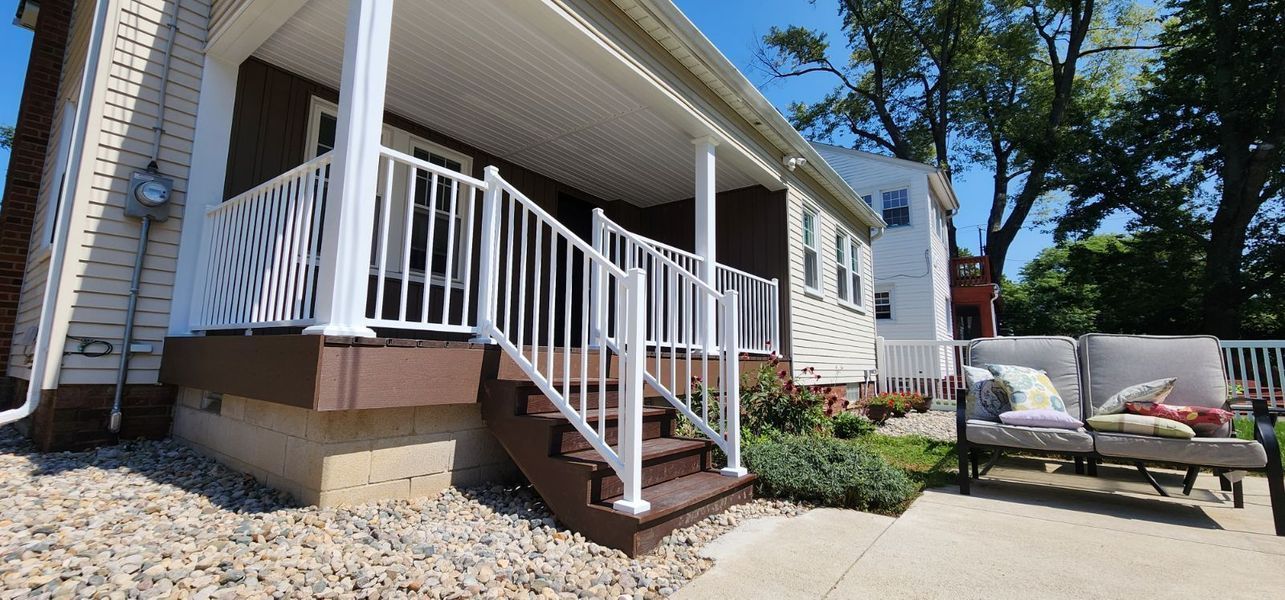 A house with a porch and steps, white railing, brown trim, and a patio with a couch.