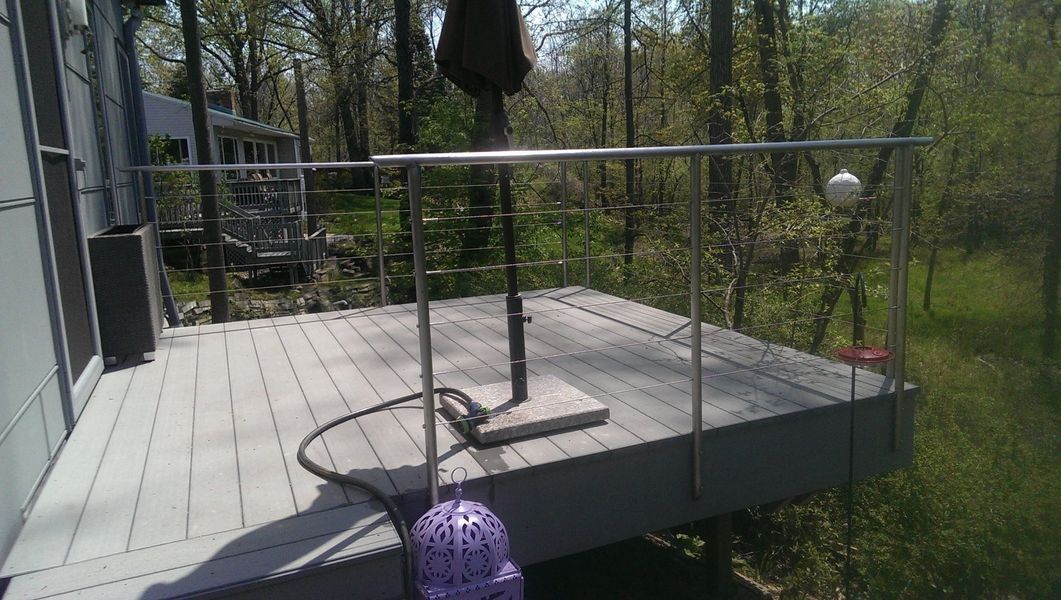 Wooden deck with a railing overlooking a wooded area. A clothesline is set up, and a hose lies on the deck.
