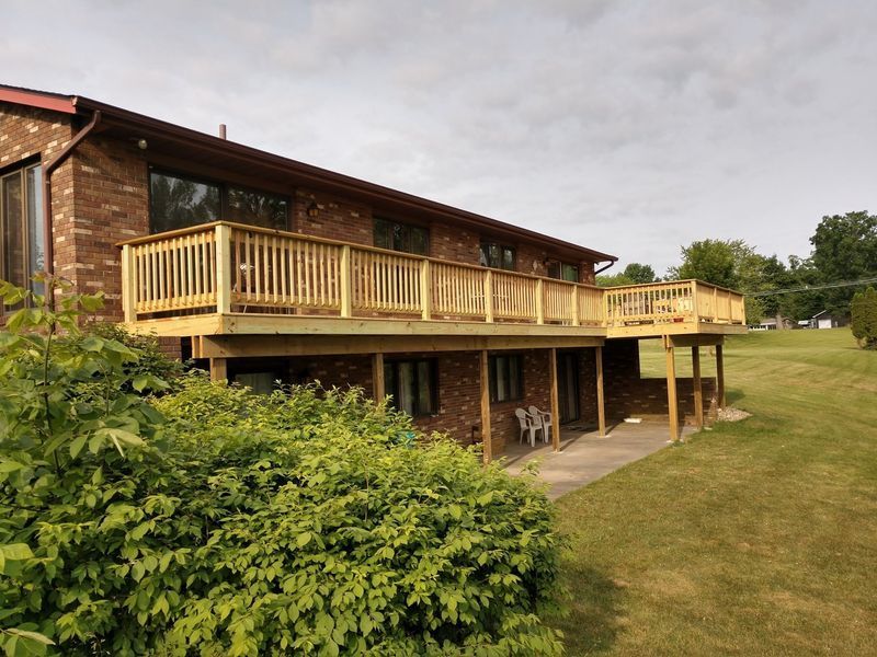 Two-story brick building with new wooden decks. Green grass and shrubs in the foreground. Overcast sky.