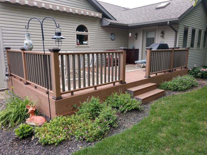 Backyard deck with brown railing, steps, and greenery. Beige house exterior.