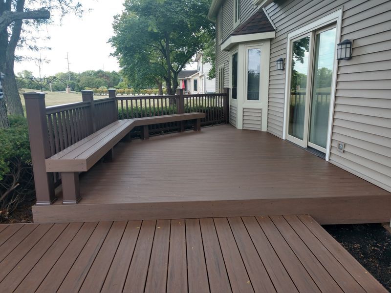 Brown composite deck with built-in bench, attached to a house with siding and a glass sliding door.