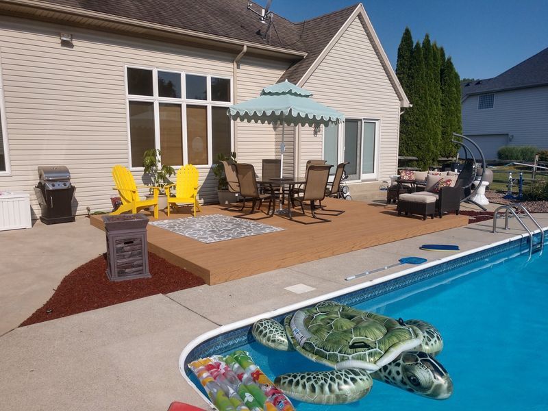 Backyard with a deck, pool, and house. Outdoor furniture, umbrella, and pool floats are visible.