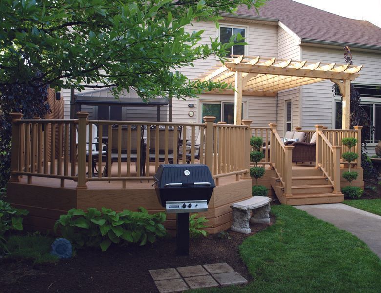 Backyard deck with pergola, grill, seating, and landscaping; steps lead to raised area.