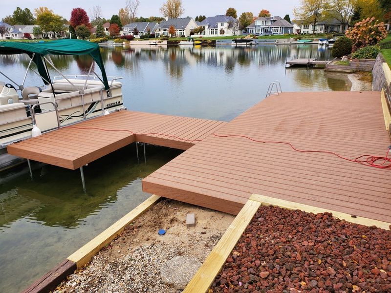 Wooden dock extending into a lake, with a boat docked on the left. Houses line the opposite shore.