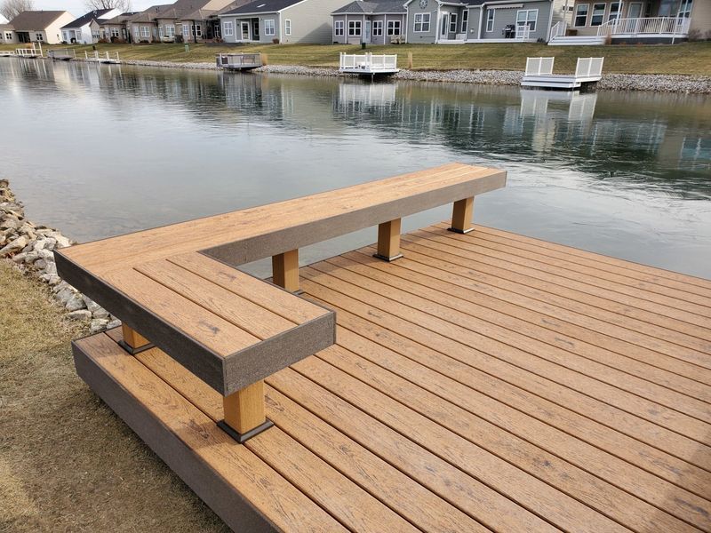 Wooden dock with a built-in bench, overlooking water and houses on the shore.