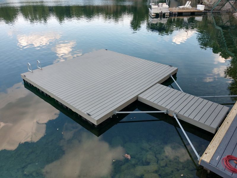 Floating gray dock with a ramp and ladder in a lake.
