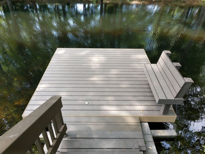 Wooden dock with bench extending into a reflective body of water.