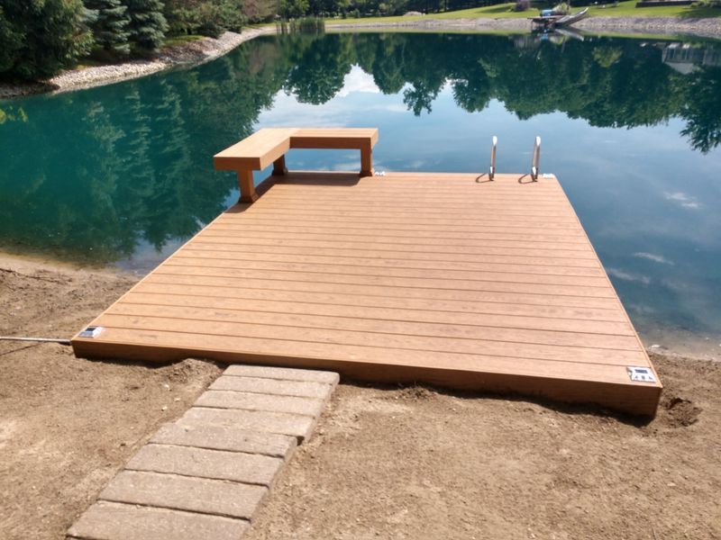 Brown composite dock with bench and ladder on a lake; brick path leads to the dock.