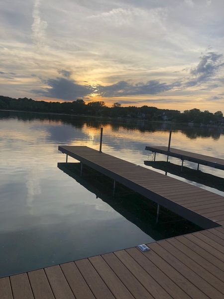 Sunset over calm lake with two docks. Orange, yellow, and blue sky reflects on the water.
