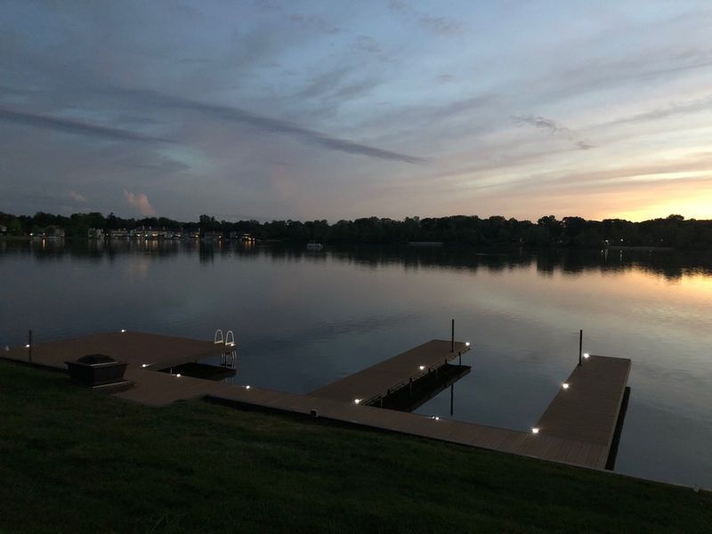 Dock on calm lake at dusk with colorful sky reflecting on water.