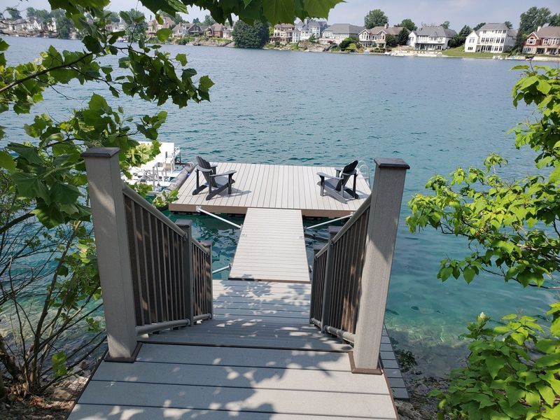 Wooden dock with stairs leading to chairs overlooking clear water and houses.