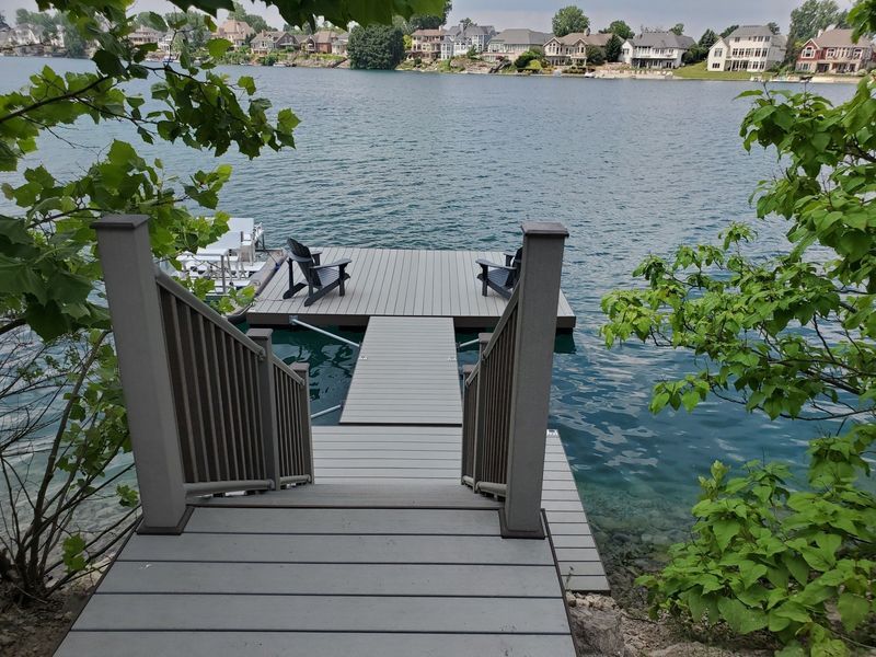 Wooden dock with stairs leading to chairs overlooking a lake.