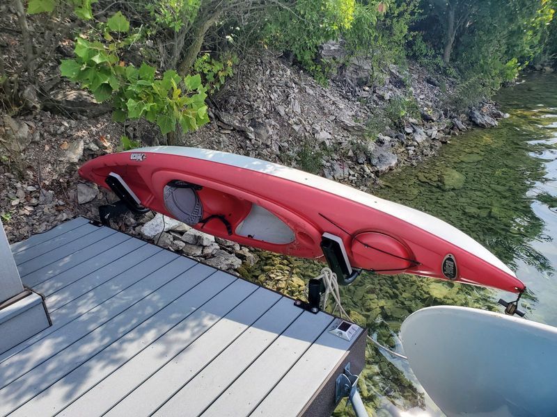 Red and white kayak mounted on a dock with a rocky shoreline and green water.