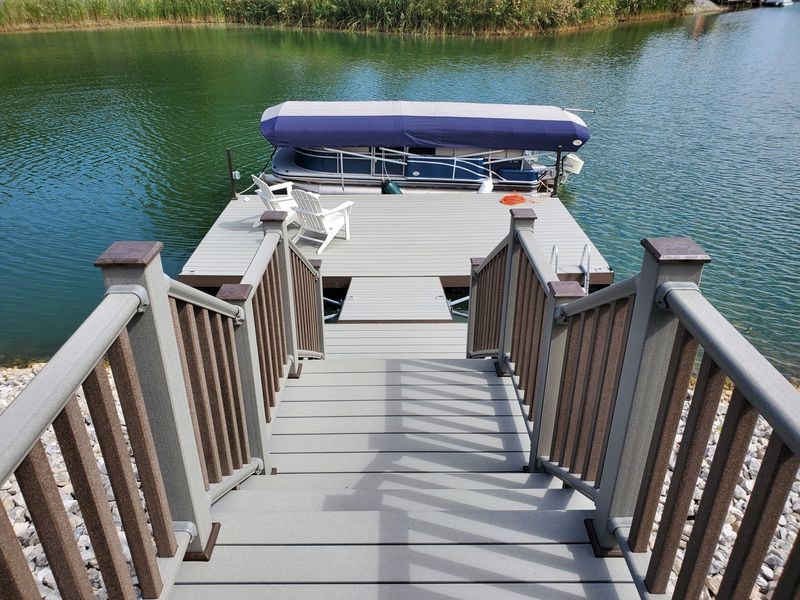Wooden dock with stairs leading to a pontoon boat covered by a blue canopy on a calm lake.