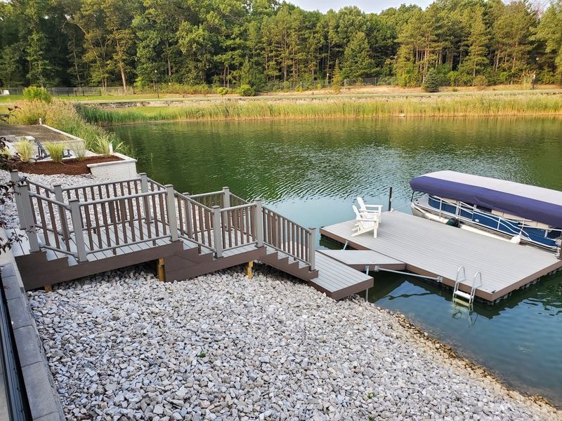 Dock with stairs leading to a lake. A pontoon boat is docked, and a white chair is present.