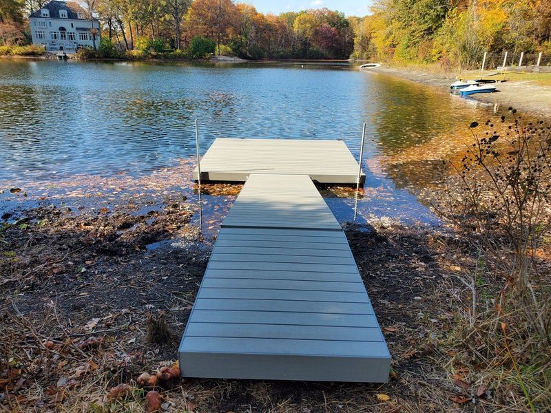 Gray dock extending into a lake, surrounded by fall foliage. A house is visible on the far bank.