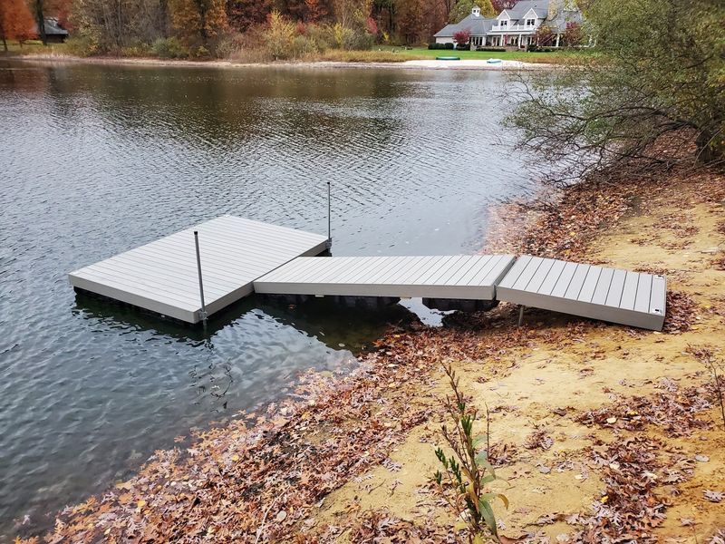Dock extending from shore into lake; gray platform and ramp, fall leaves on the bank.