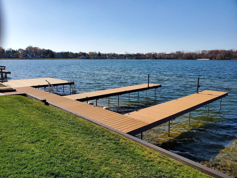 Lakefront docks extending into blue water under a clear sky. Green lawn in foreground.