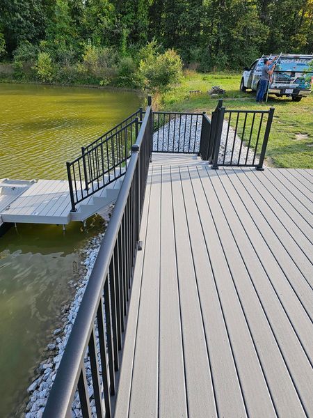 Black railing and gate on a composite deck overlooking a pond. A truck sits in the background.
