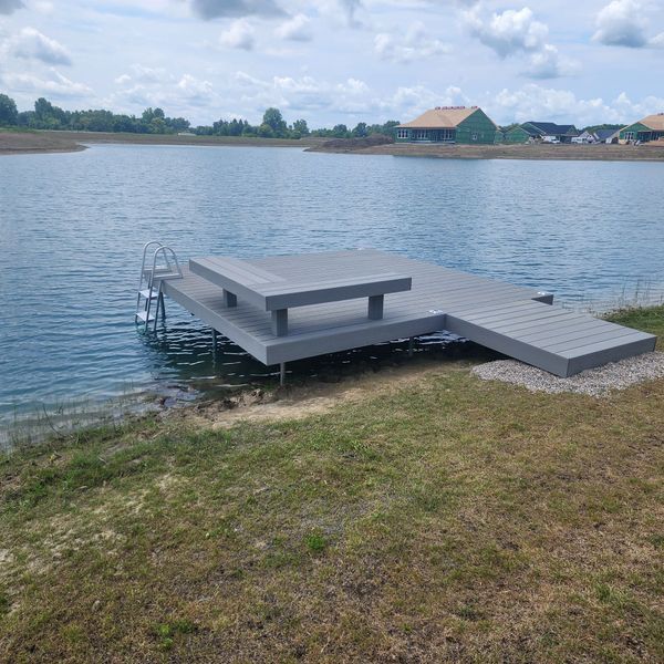 Grey composite dock with seating and ladder extending into a blue lake.