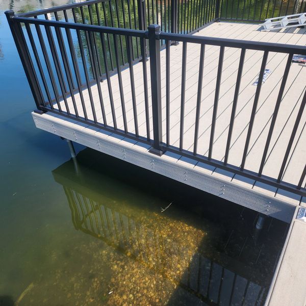 Deck with black railing over water, supported by pilings.