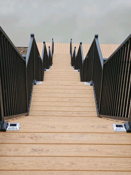 Wooden dock stairs leading down to water, black metal railings, and solar lights.