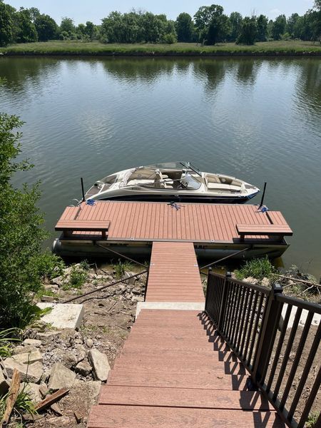 A boat docked at a pier, accessed by wooden stairs. The lake reflects the sky and trees.
