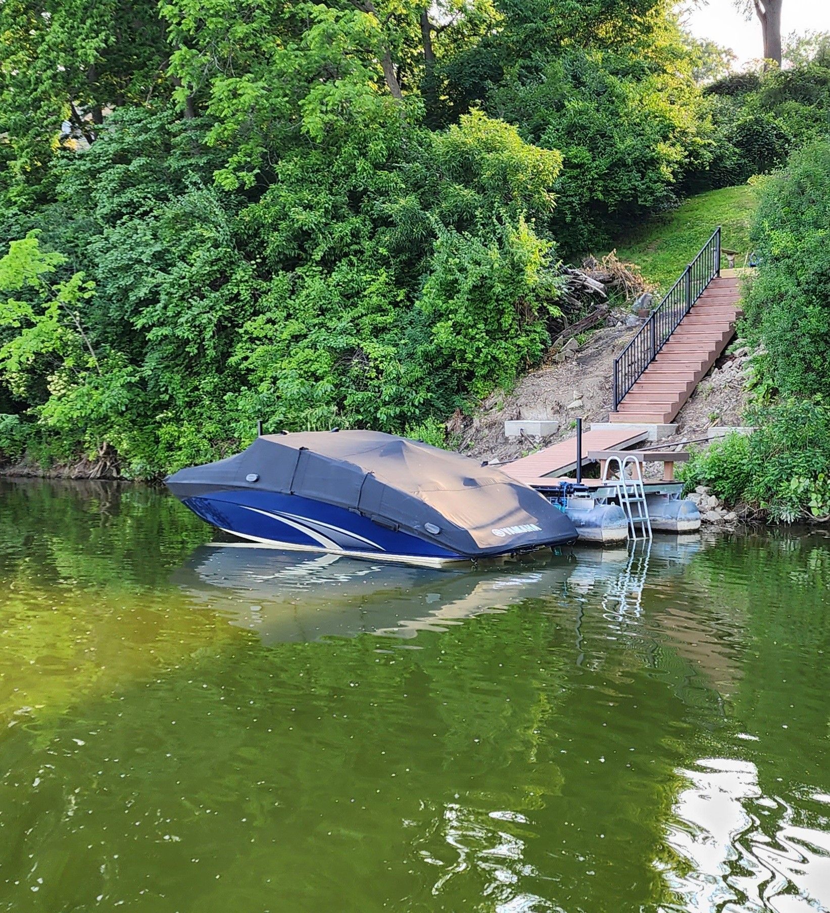 Boat covered with blue tarp on a dock with stairs leading up to trees on a hillside.