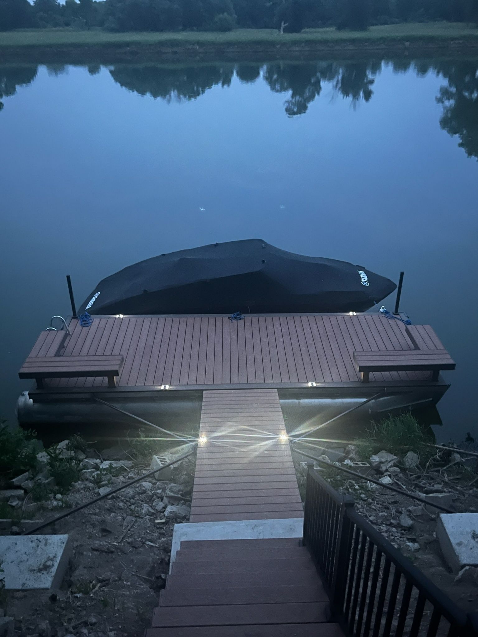 Dock on calm water, boat covered, wooden pathway leading to it, dusk setting.