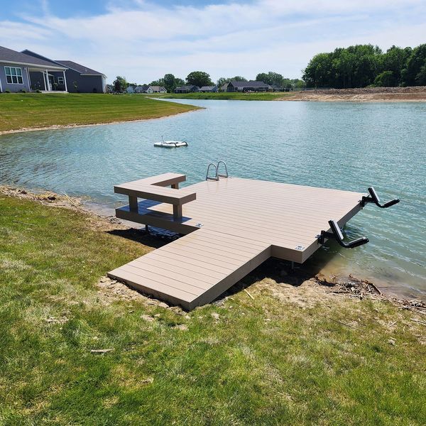 A composite dock extends into a lake, with a boat lift, stairs, and a built-in bench.