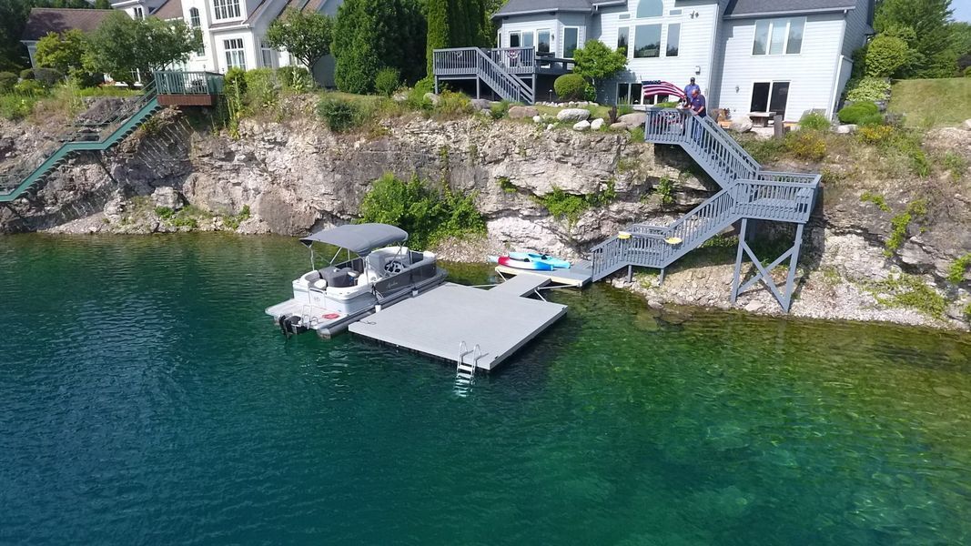 Dock with a boat and stairs leading to a lakefront house. Grey and blue colors.