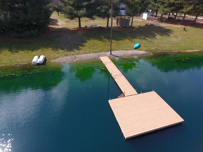 Dock extending into a blue lake, with a small beach and grassy bank in the background.