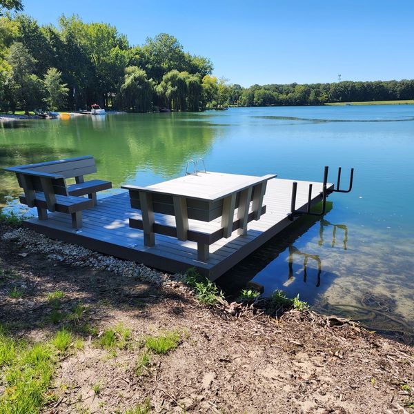 Dock with picnic table on a lake. Clear water, trees in background, sunny day.
