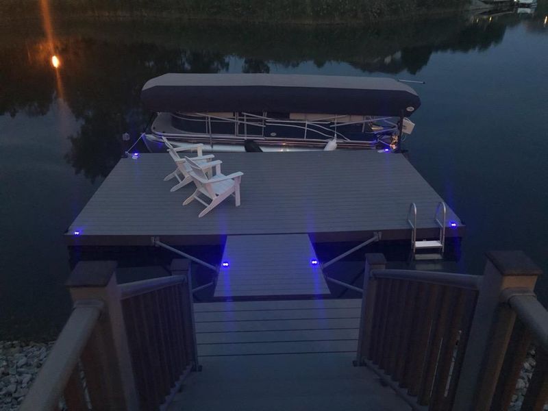 Dock with pontoon boat, two white chairs, lit blue steps, and a canopy at dusk.