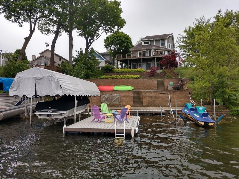 Lakeside home with boat dock and colorful chairs. Boat cover and jet ski on the water.