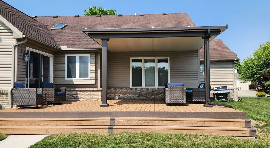 A composite deck with a covered patio attached to a house with outdoor furniture.
