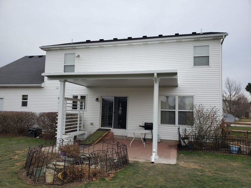 Back of a two-story white house with a patio roof and a small backyard with a fire pit.