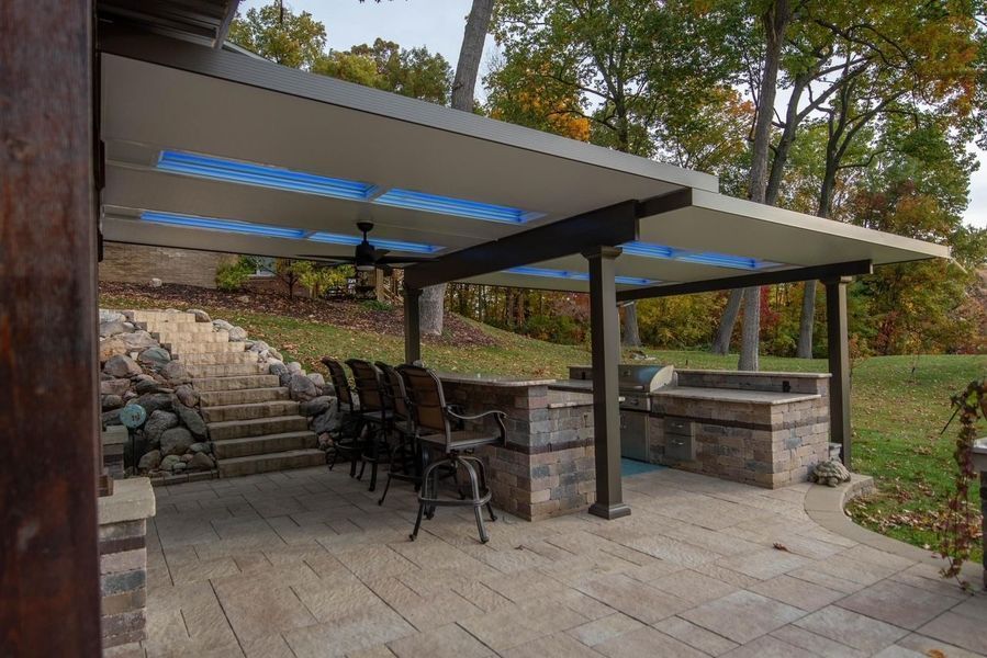 Outdoor patio with kitchen, bar, and covered seating. Features stone walls, stairs, and a ceiling fan.